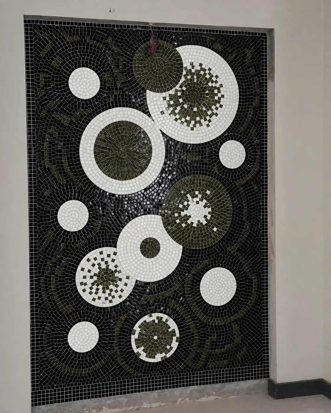 Abstract black, white and dark-olive circular vitreous glass mosaic installed in a recessed wall niche.